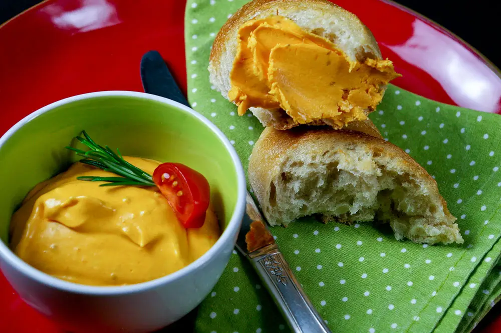 Tomatenbutter, hergestellt aus den Tomaten von meinem Rezept „confierte Tomaten“ und Butter. Angerichtet auf einem roten Teller mit grüner Serviette, sieht die wunderschöne orangefarbene Tomatenbutter in ihrem grünen Töpfchen, wunderschön aus.