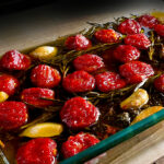 Confierte Tomaten, in einer Auflaufform liegen rote Cocktailtomaten mit Kräutern und Knoblauch, langsam gegart in Olivenöl.